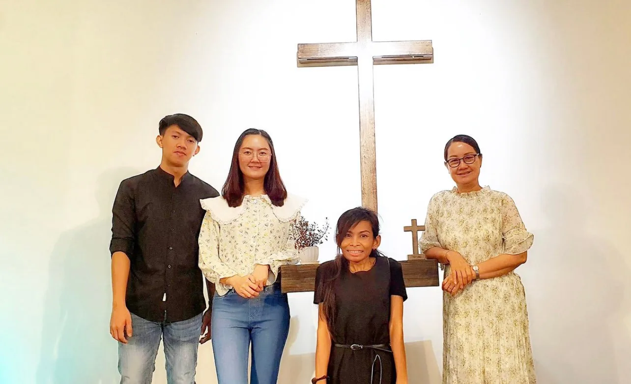 Naleng Real with three others in front of a wooden cross at church