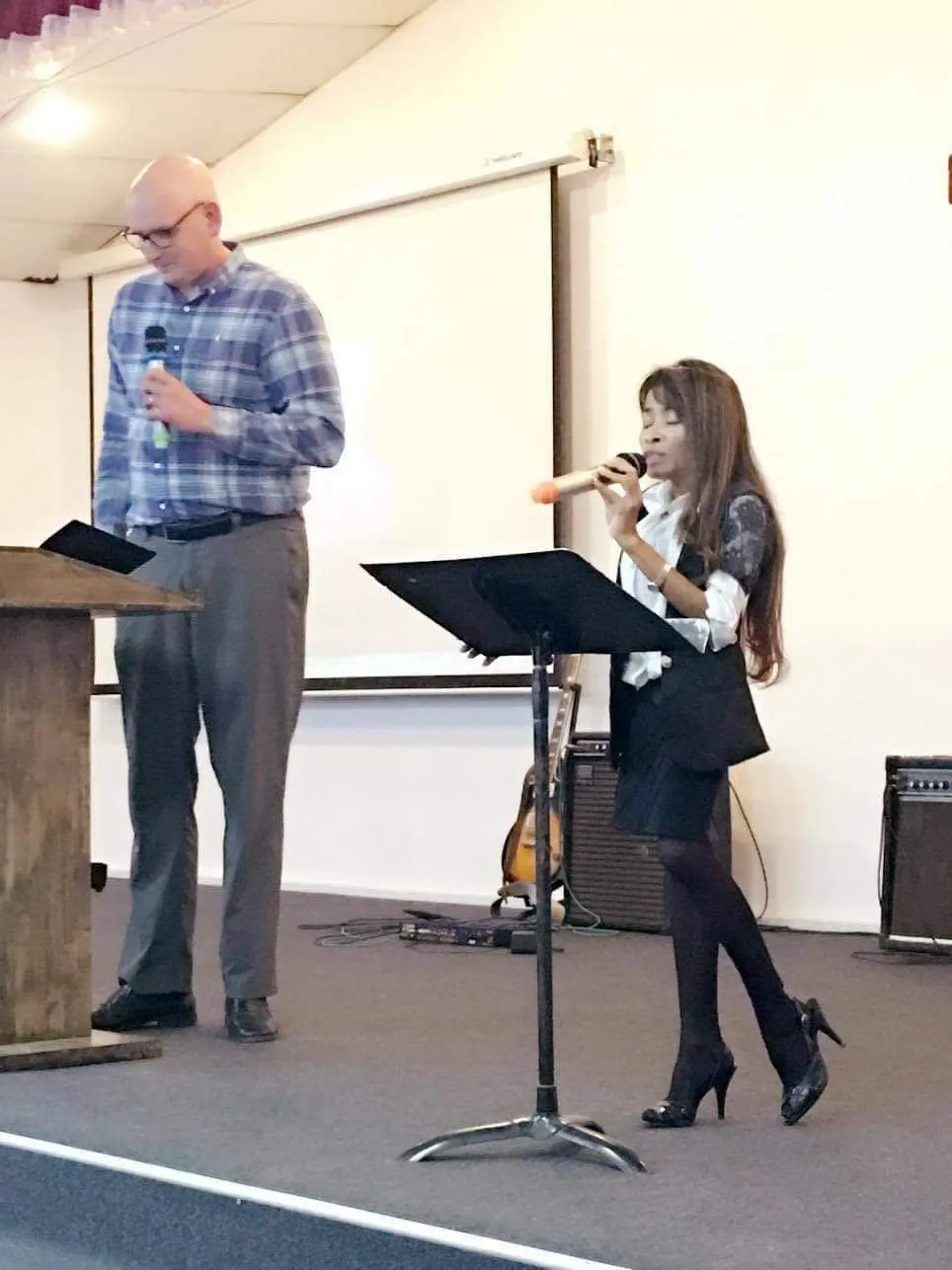 Naleng Real interpreting at a music stand beside a speaker in a church hall