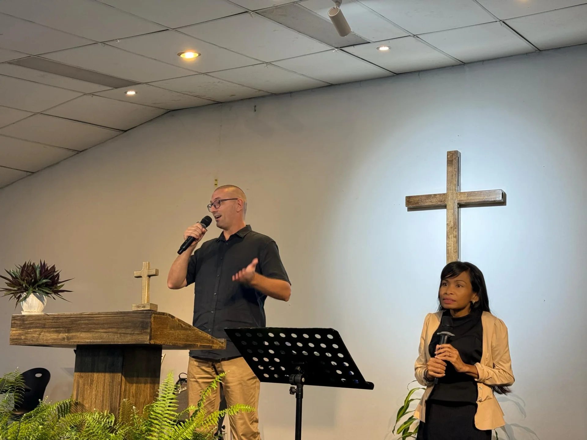 Naleng Real standing beside a speaker at a church podium, microphone in hand, waiting to interpret