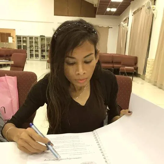 Naleng Real translating a text by hand into a notebook written in Khmer script