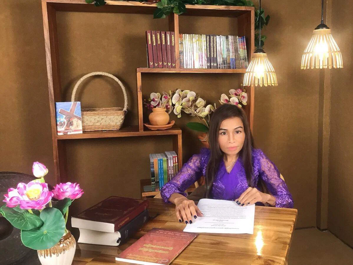 Naleng Real seated at a wooden desk with a script and Khmer Bibles, ready to record