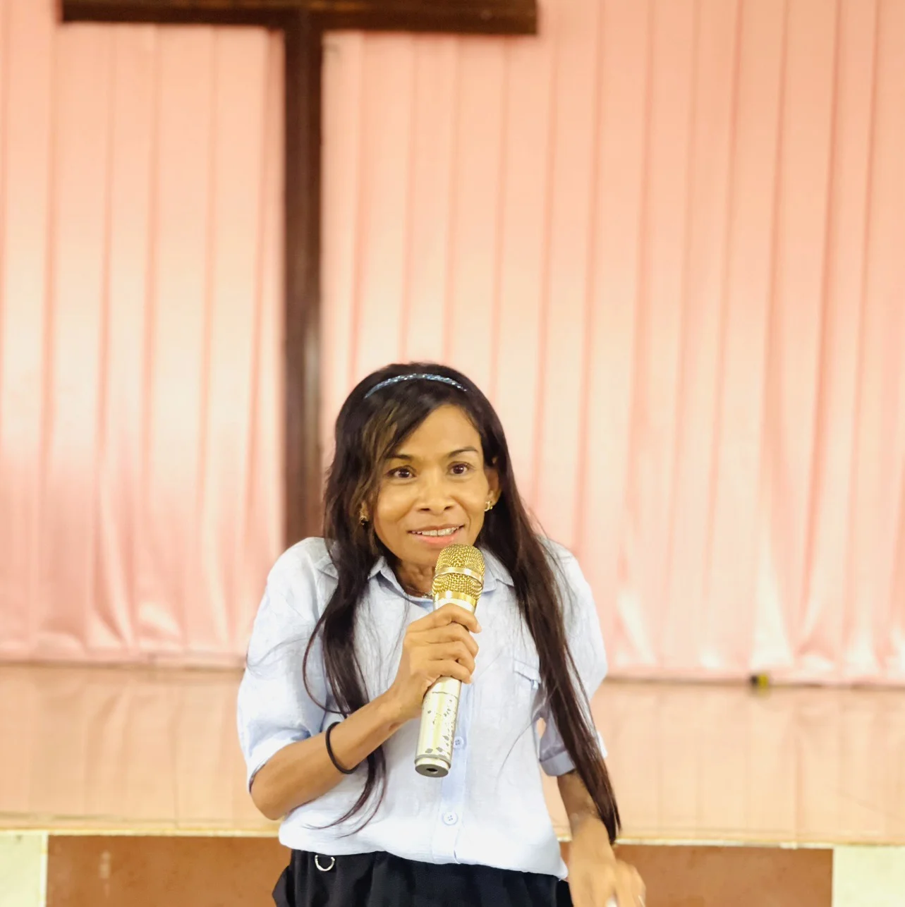 Naleng Real holding a microphone in front of a curtained hall